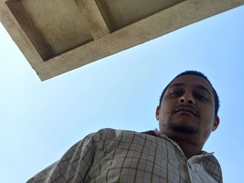 Low angle portrait of young man against clear sky on sunny day