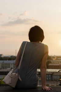A lonely woman looks at city at sunset from the observation deck, rear view.