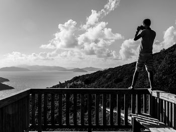 Man photographing through camera while standing on railing at observation point