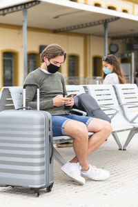 Full length of man using mobile sitting outdoors