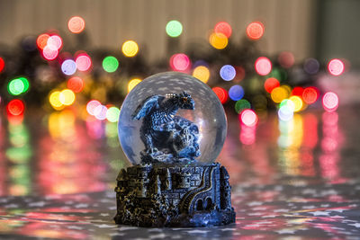 Close-up of snow globe with illuminated christmas tree in background