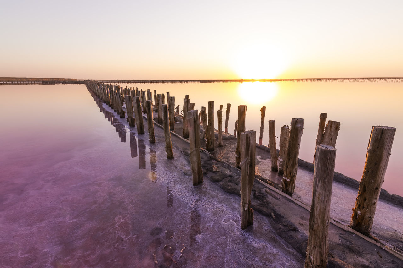 water, sky, sunset, sea, scenics - nature, beauty in nature, tranquility, nature, tranquil scene, land, wood, horizon over water, sun, horizon, dawn, beach, landscape, wooden post, environment, reflection, idyllic, evening, shore, no people, pier, post, ocean, twilight, clear sky, seascape, in a row, coast, sunlight, outdoors, travel destinations, non-urban scene, wave, travel, urban skyline, coastline, architecture, jetty