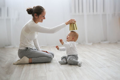 Funny baby 10 months with his mother playing with a pot in the kitchen, lifestyle 