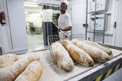 Baker taking out freshly baked bread from the oven of a bakery