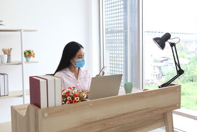 Young woman using phone while sitting on table