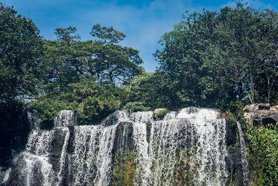 Scenic view of waterfall in forest against sky