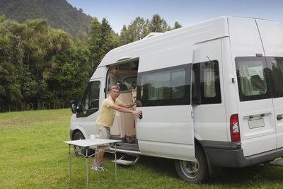 Full length portrait of man opening van door on field