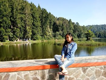 Young woman sitting by lake against sky in situgunung sukabumi.