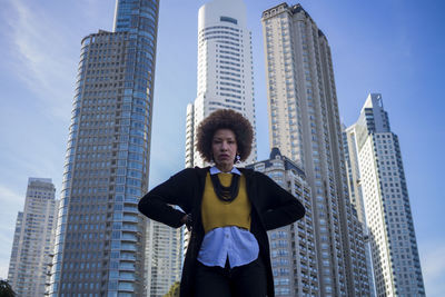 Low angle portrait of woman standing against modern buildings in city