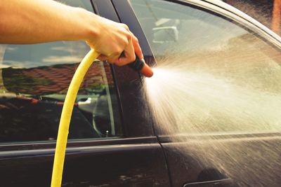 Cropped image of man washing car with gardening hose