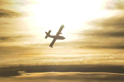 Low angle view of silhouette airplane flying against sky during sunset