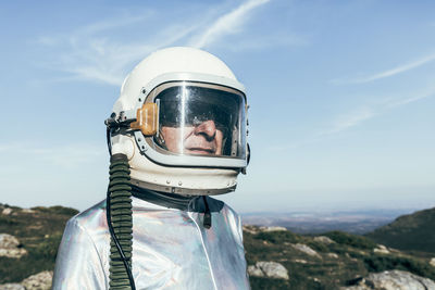Male astronaut in spacesuit and helmet standing on grass and stones in highlands