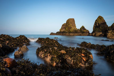 Scenic view of rocks in sea against clear blue sky