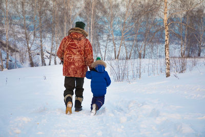 Rear view of father and son walking on snow covered landscape