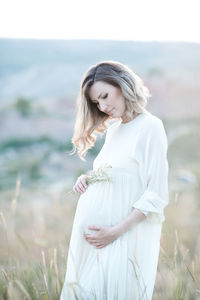Pregnant woman holding belly standing on field