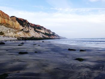 Scenic view of cliff by beach against sky