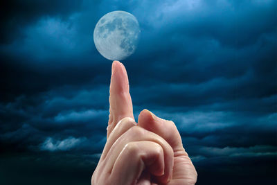 Digital composite image of hand holding moon against cloudy sky