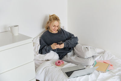Side view of young woman sitting on bed at home