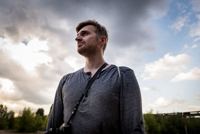 Low angle view of young man with camera against cloudy sky