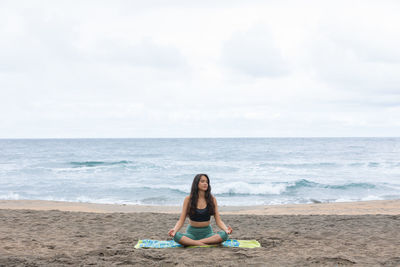 Rear view of woman sitting on beach against sky