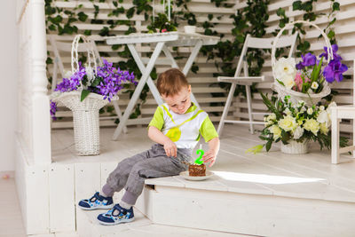 Full length of boy sitting by potted plants