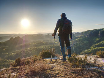 Disabled man with crutches stands on a big rock and looking to mountains at horizon. heavy walk