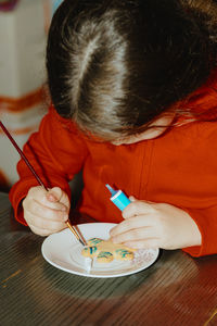 One girl is coloring cookies while sitting at the table.