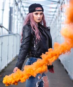 Portrait of young woman holding smoke bomb on bridge