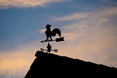 Low angle view of silhouette weathercock on roof