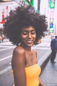 Shy young woman with afro hairstyle standing on city street
