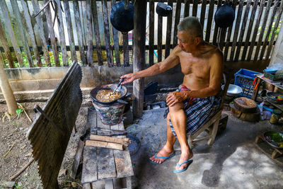 Full length of senior man cooking while sitting on chair