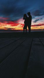 Silhouette couple standing on orange sunset sky