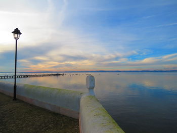 Street light on promenade by river against sky during sunset