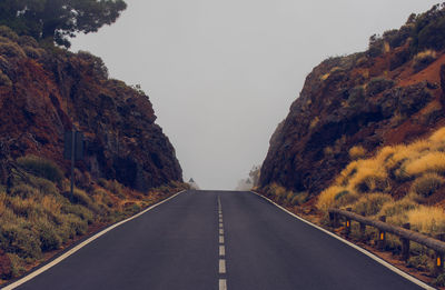 Empty road amidst mountains against clear sky