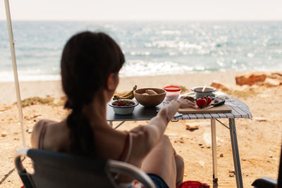 Rear view of woman sitting by food on table at beach