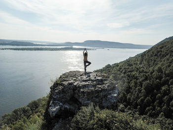 Man standing on rock by sea against sky