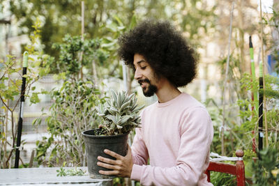 Young man looking away while standing on potted plants