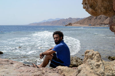 Portrait of man sitting at beach against clear sky