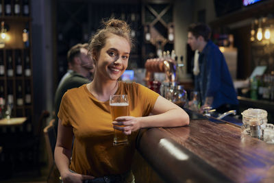 Portrait of young woman holding beer at bar