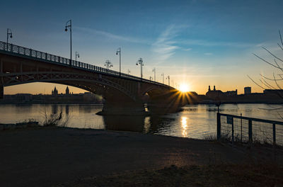 Bridge over river in city against sky during sunset