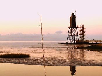 Silhouette lighthouse by sea against sky during sunset