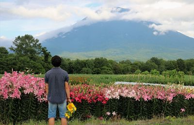 Rear view of person standing on field against cloudy sky