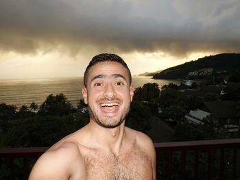 Portrait of happy shirtless man against sea during sunset