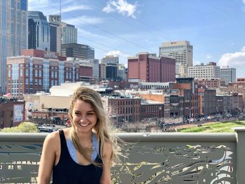 Portrait of smiling young woman standing against buildings in city