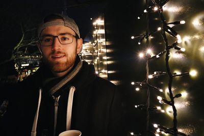 Portrait of young man against illuminated lights at night