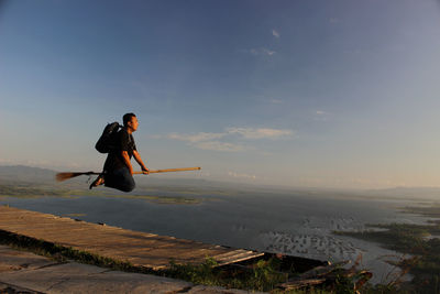 Side view of man flying on broom against sea and sky during sunset