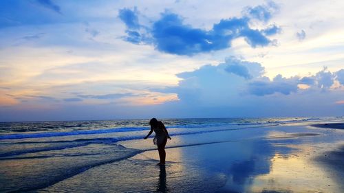 Silhouette woman standing at beach against sky during sunset