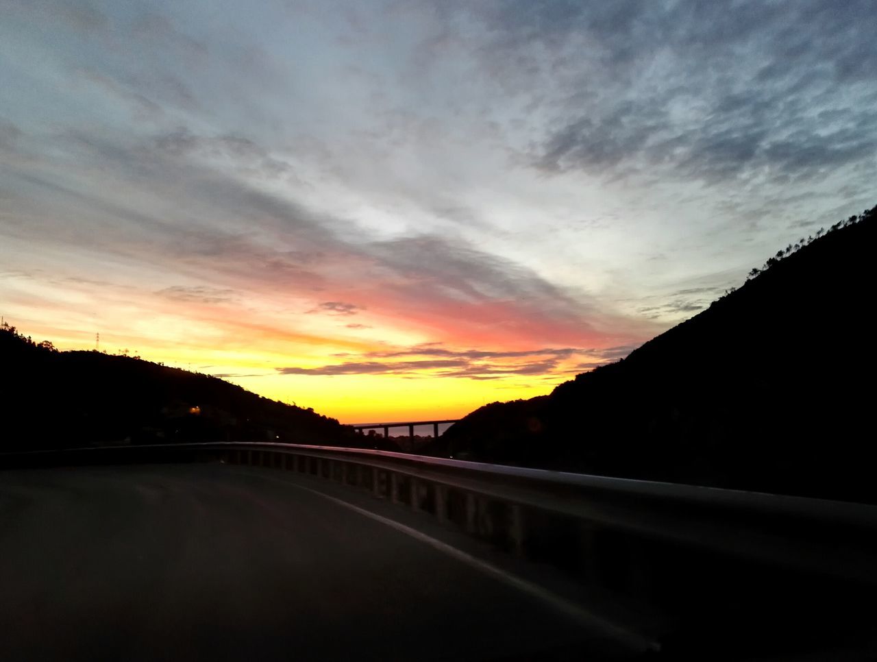 sunset, sky, cloud - sky, tranquility, orange color, scenics, tranquil scene, the way forward, beauty in nature, silhouette, mountain, cloud, nature, road, water, built structure, idyllic, dusk, cloudy, railing