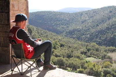 Side view of man sitting on seat against mountain range