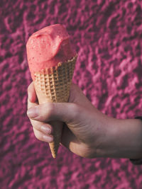 Cropped hand of boy holding ice cream cone against wall